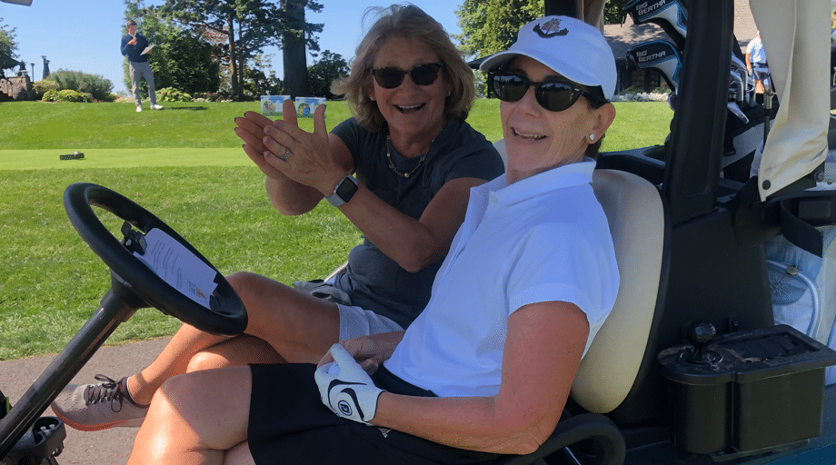 two women in golf cart smiling and clapping