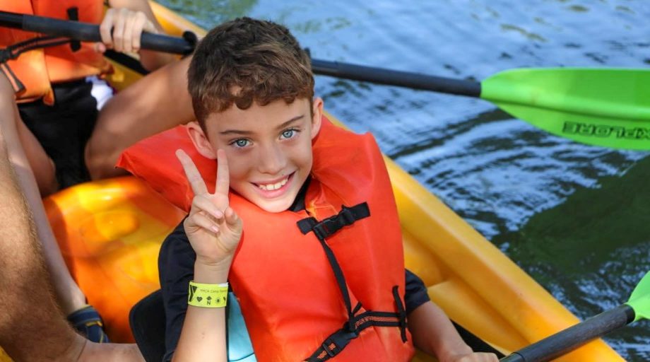 YCMA camper giving peace sign while kayaking
